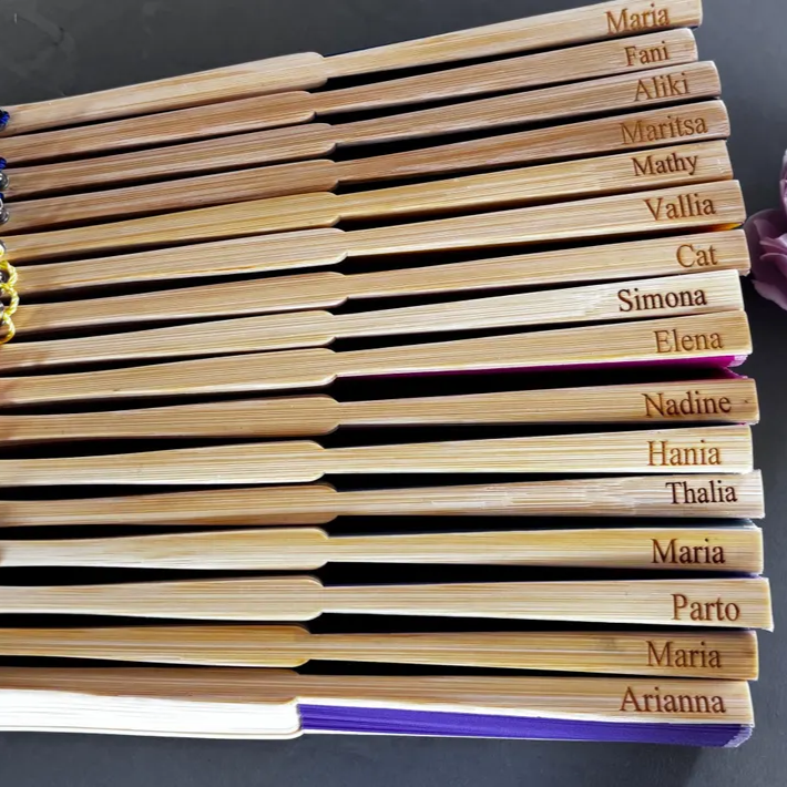 Custom engraved bamboo hand fans personalised with individual names, arranged in a stack for bridesmaids or event gifts.