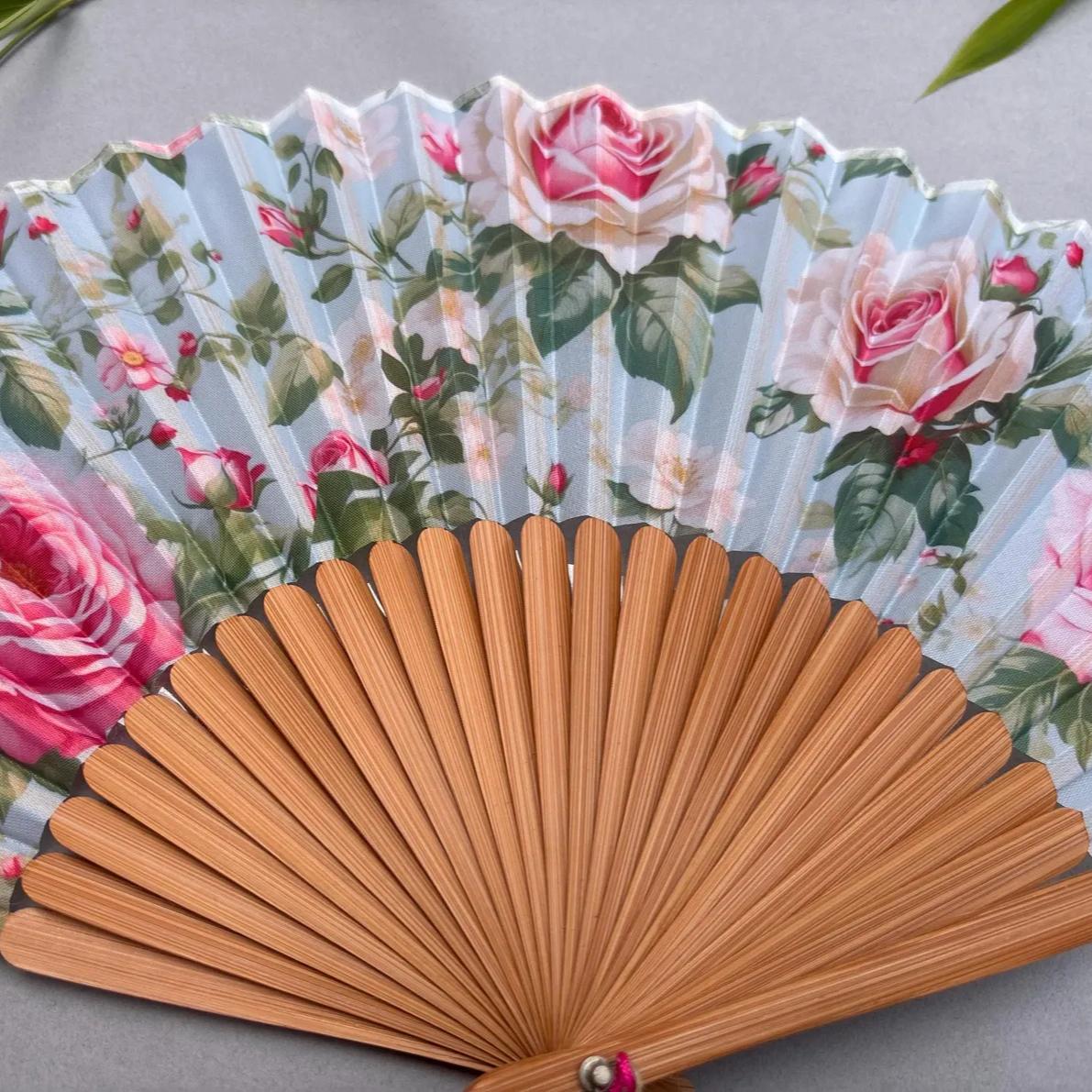 Floral-patterned hand fan with pink roses on a gray background