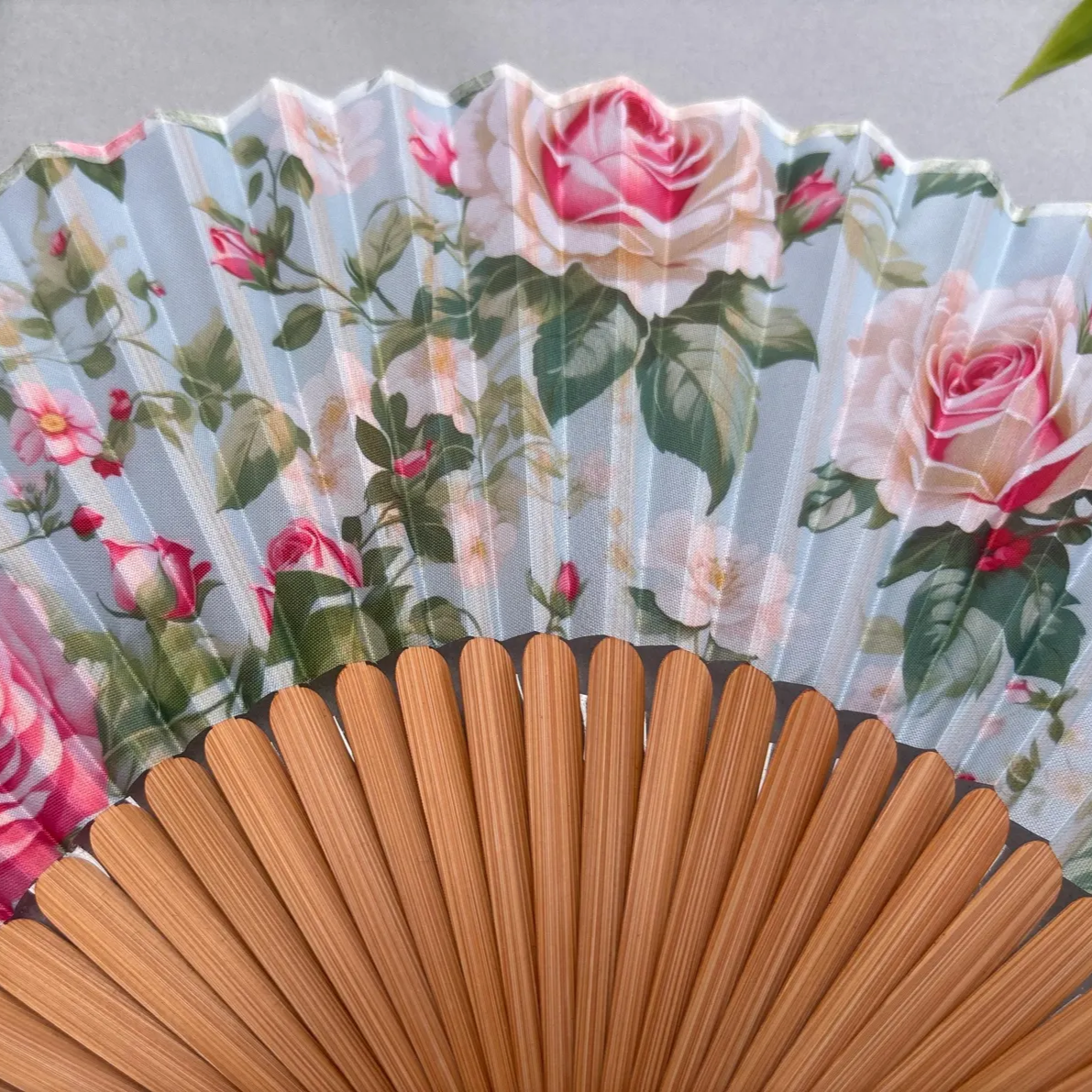 Floral-patterned hand fan with pink roses on a gray background