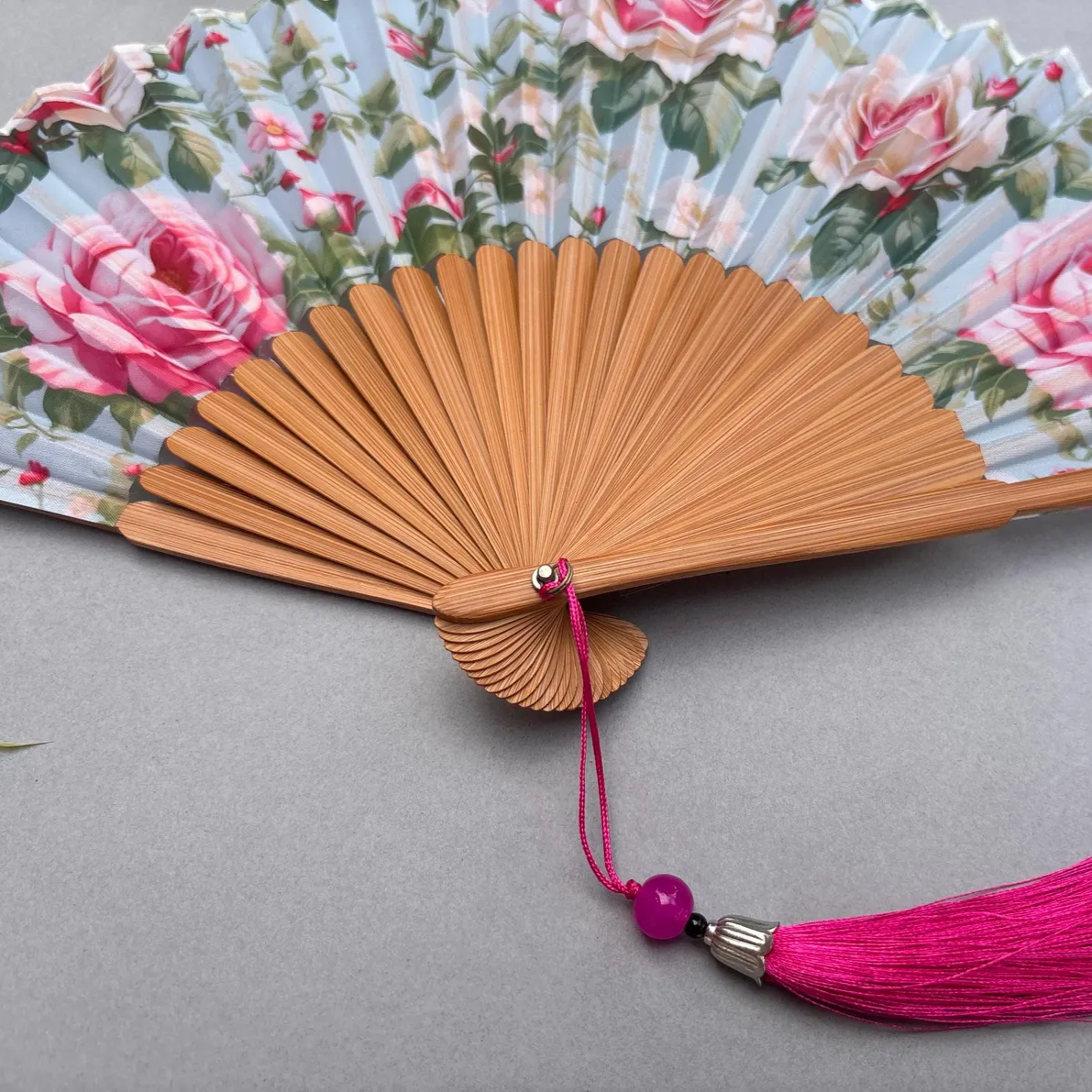 Floral-patterned hand fan with pink roses on a gray background