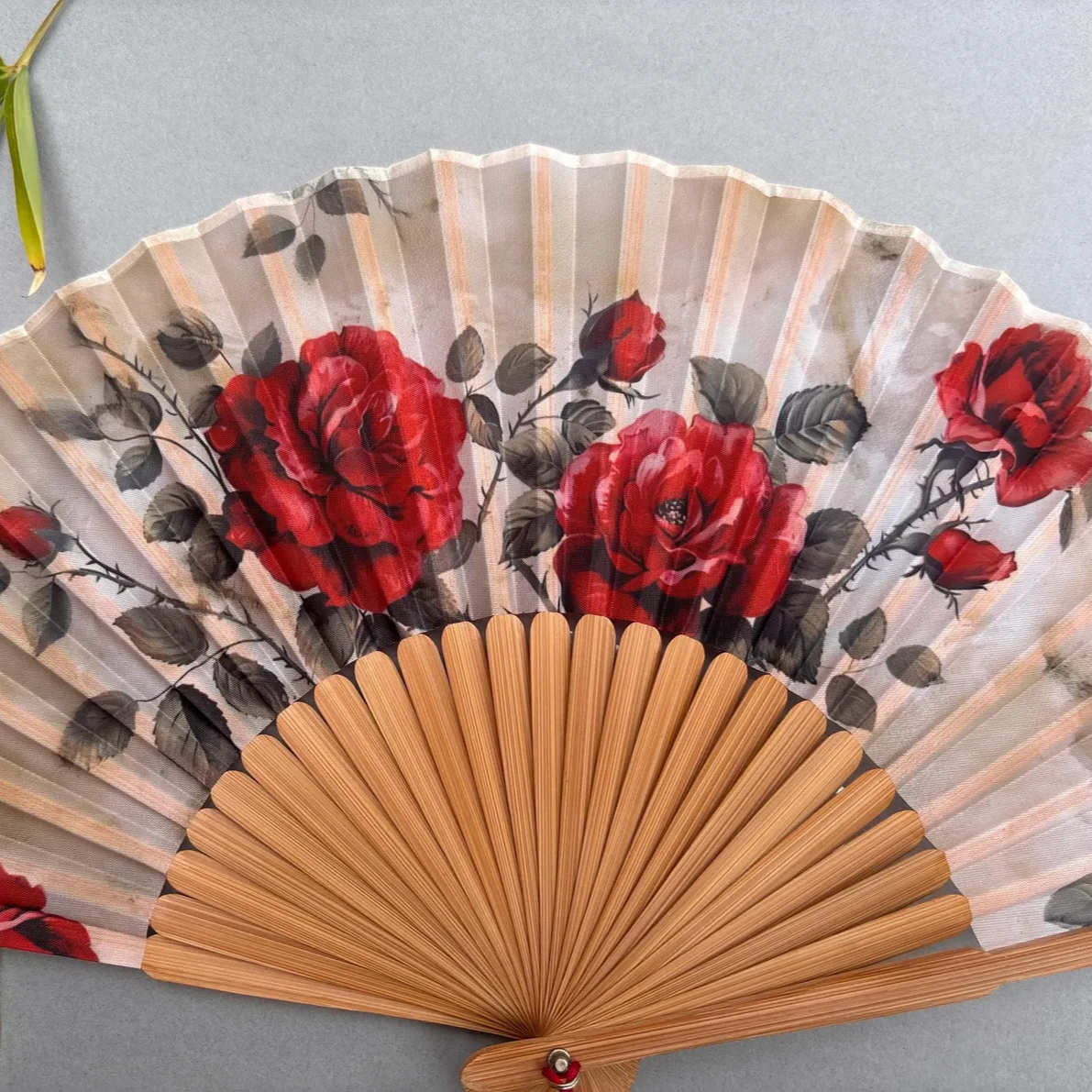 Handheld fan with red floral design on a gray background