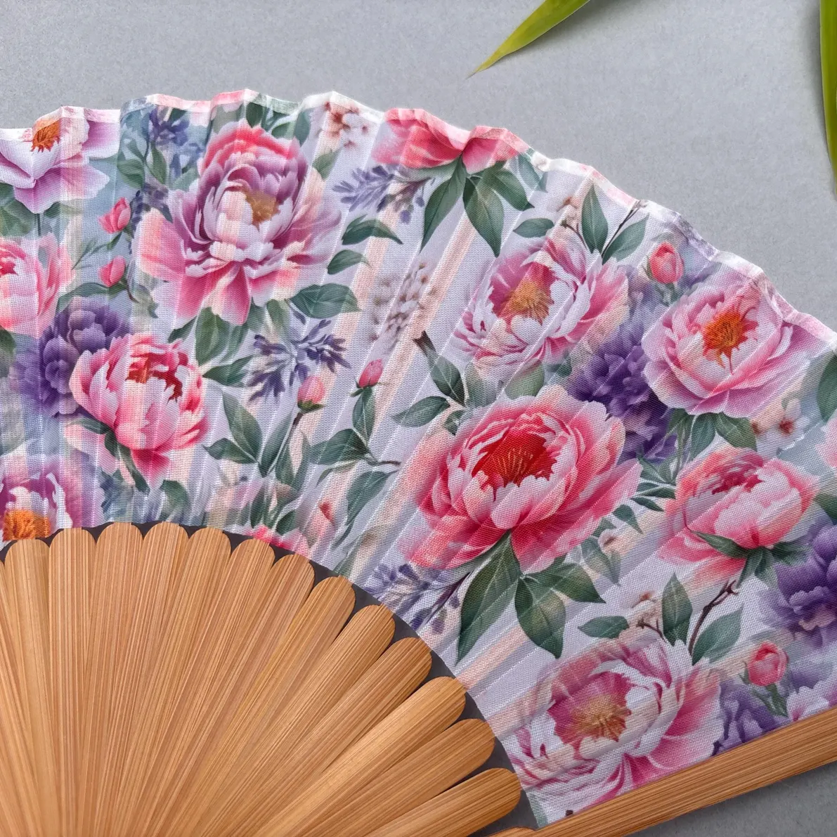 Floral-patterned hand fan with pink tassel on a gray background