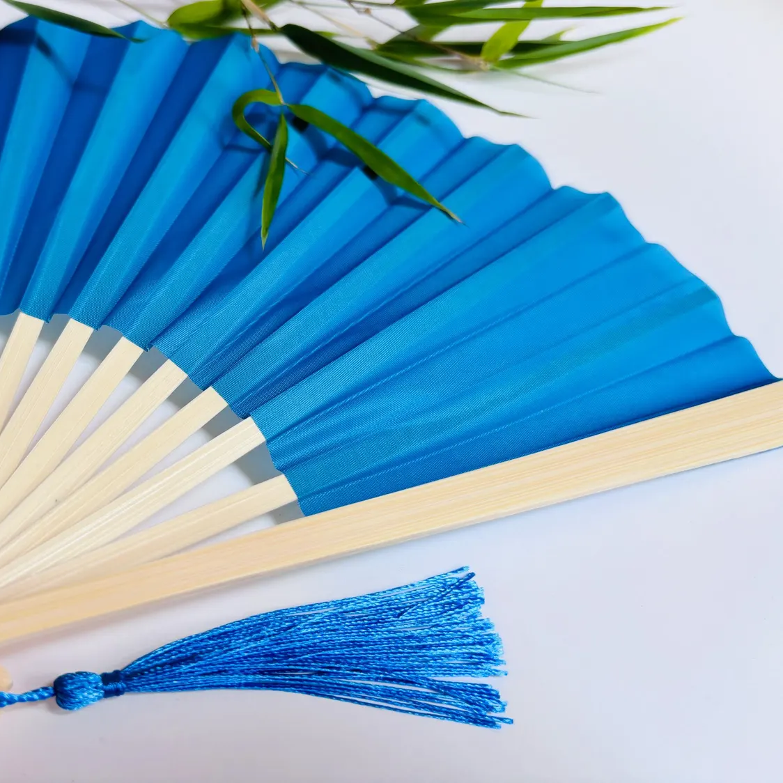 Baby Blue hand fan with a tassel on a light background