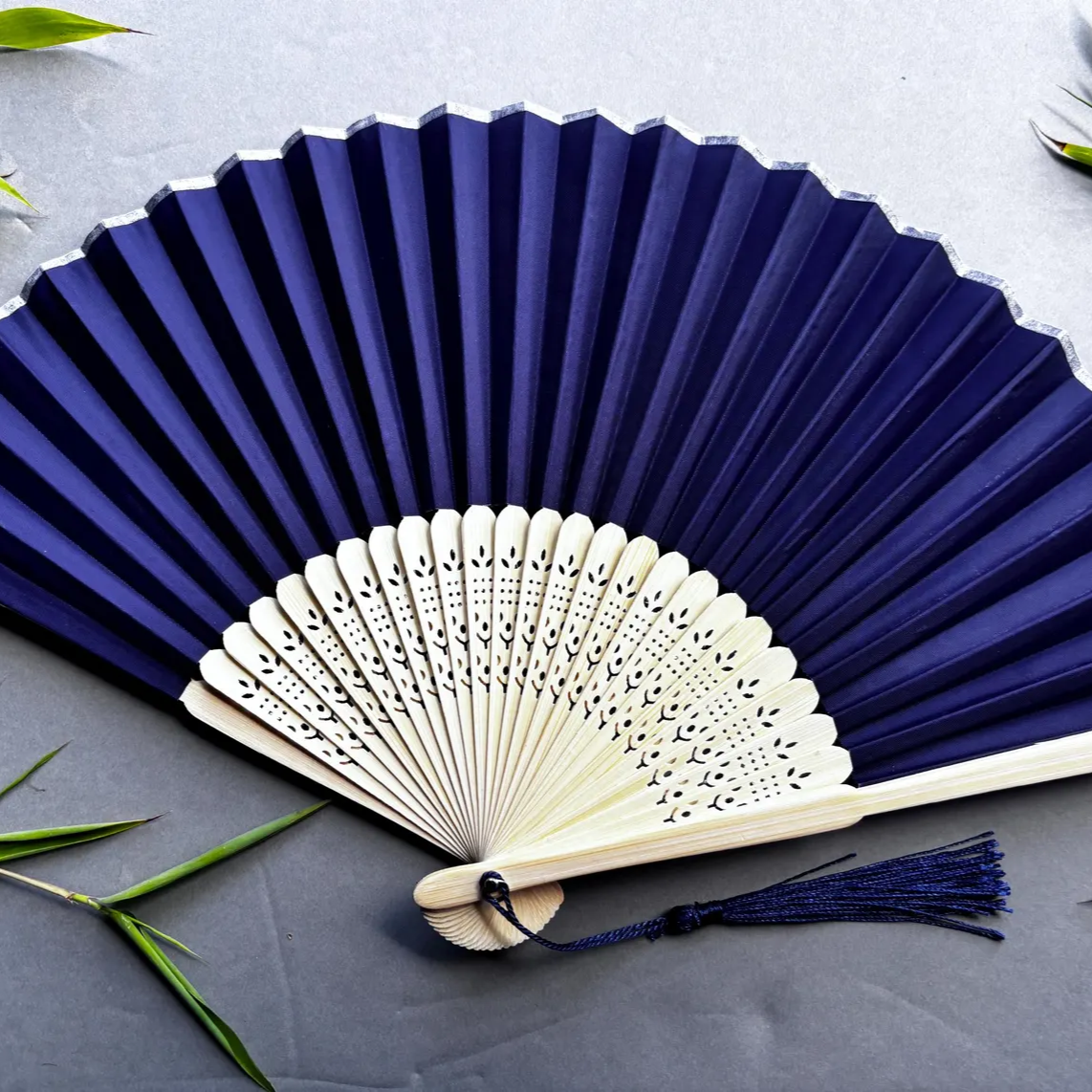 Blue and white hand fans on a gray surface with green leaves.