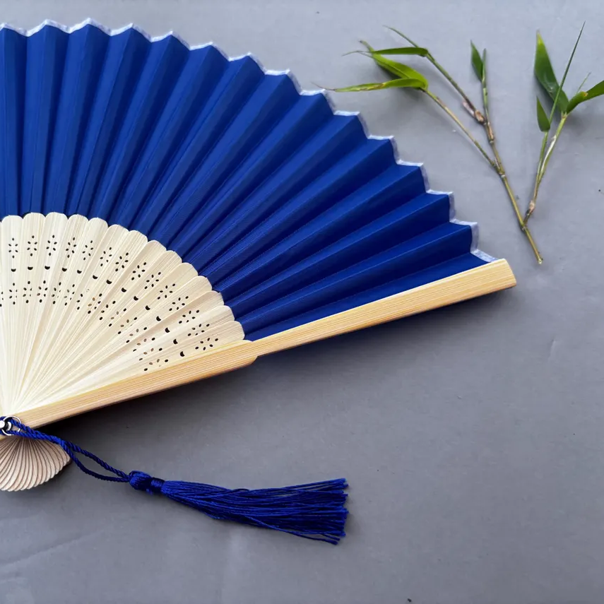 Blue and white hand fan with tassel on a gray background