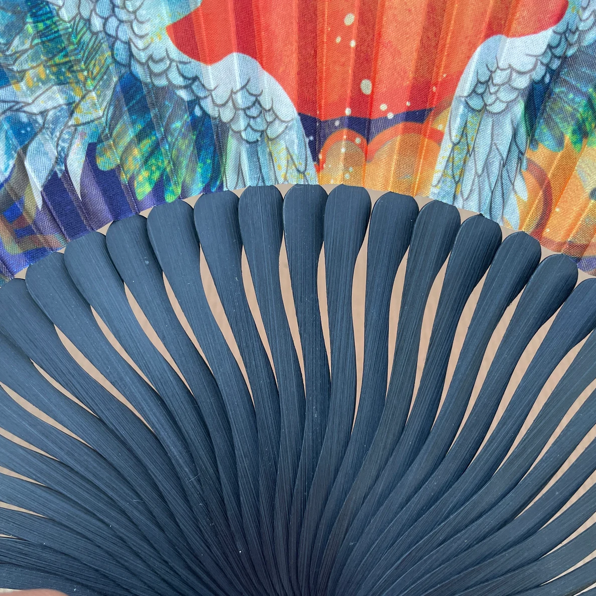 Close-up of a blue fan with colorful peacock feathers in the background