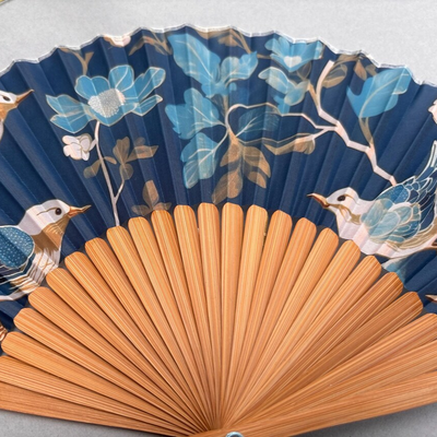 Decorative fan with floral and bird design on a gray background