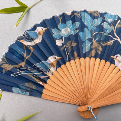 Decorative fan with floral and bird design on a gray background