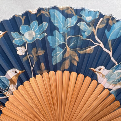 Decorative fan with floral and bird design on a gray background