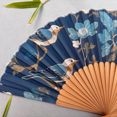 Decorative fan with floral and bird design on a gray background