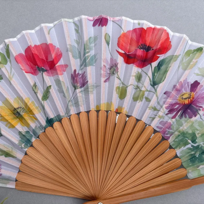 Handheld fan with floral design and red tassel on a gray background