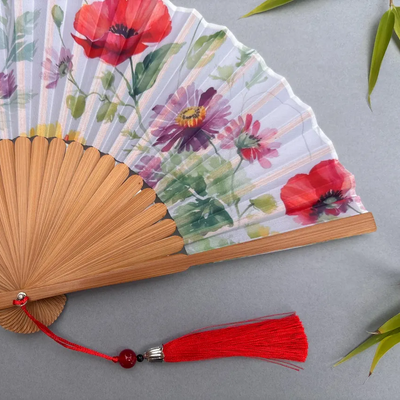 Handheld fan with floral design and red tassel on a gray background