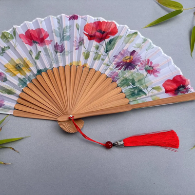 Handheld fan with floral design and red tassel on a gray background
