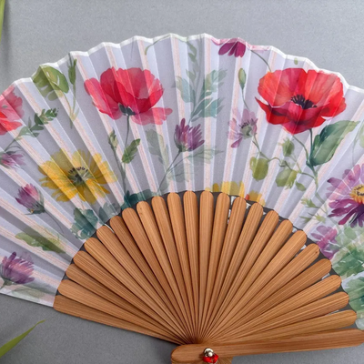 Handheld fan with floral design and red tassel on a gray background