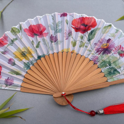 Handheld fan with floral design and red tassel on a gray background