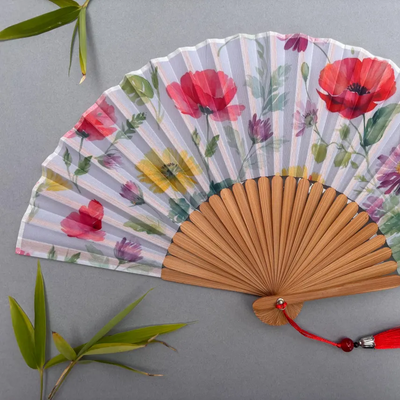 Handheld fan with floral design and red tassel on a gray background