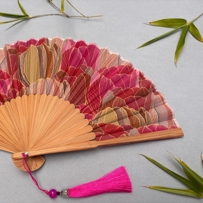 Decorative hand fan with floral design and pink tassel on a white background