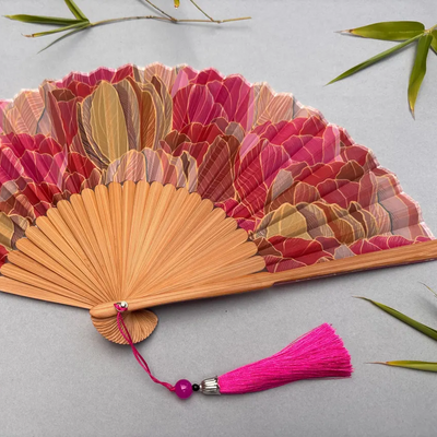 Decorative hand fan with floral design and pink tassel on a white background