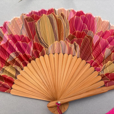Decorative hand fan with floral design and pink tassel on a white background