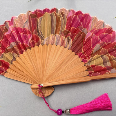 Decorative hand fan with floral design and pink tassel on a white background