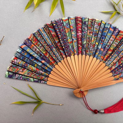 Colorful hand-fan with bamboo structure and decorative tassel on a light gray background