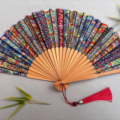 Colorful hand-fan with bamboo structure and decorative tassel on a light gray background
