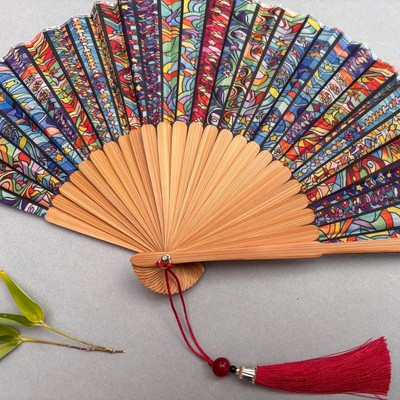 Colorful hand-fan with bamboo structure and decorative tassel on a light gray background