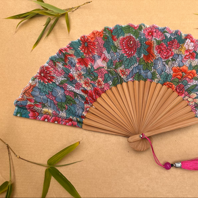 Floral patterned hand fan with a pink tassel on a gray background