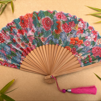 Floral patterned hand fan with a pink tassel on a gray background
