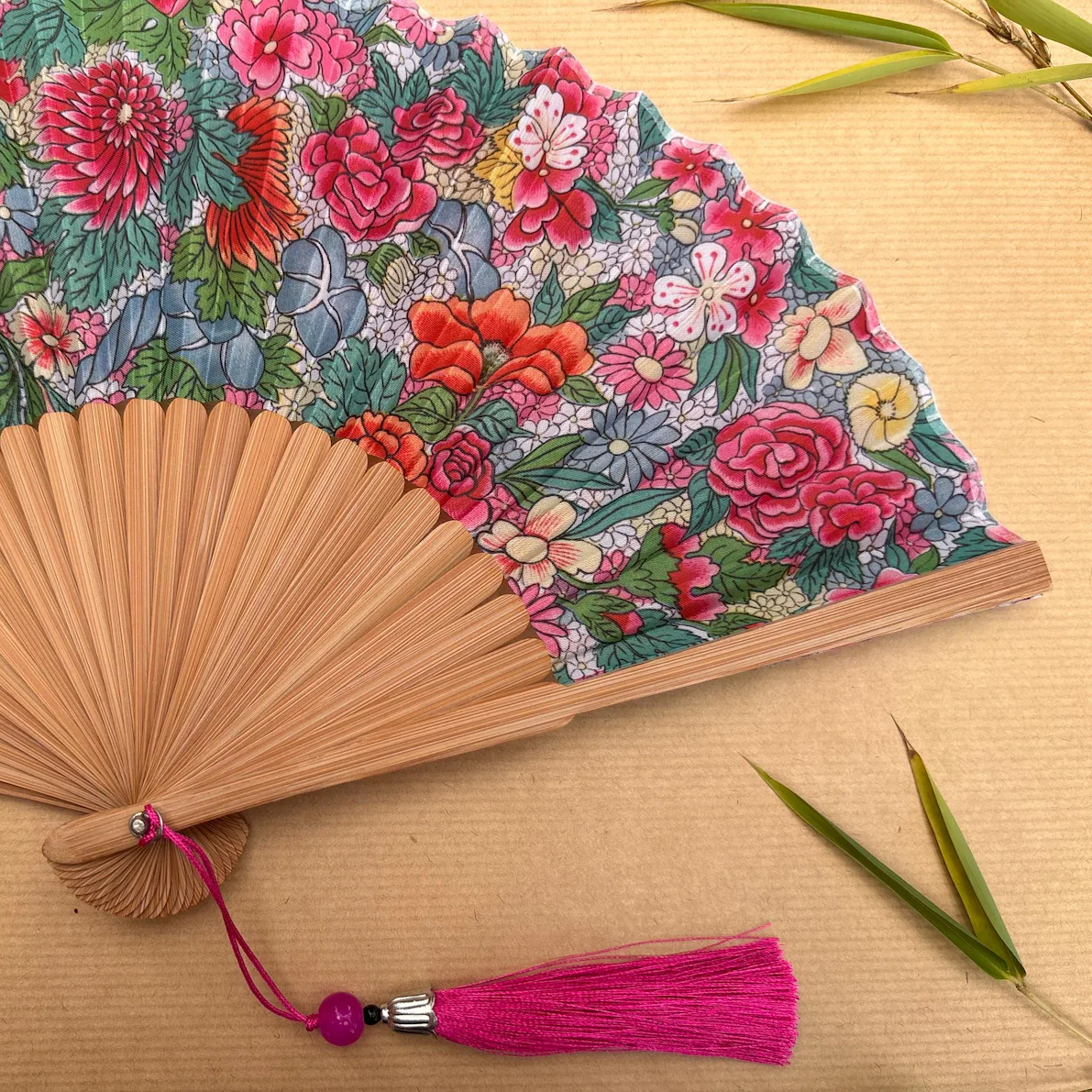 Floral patterned hand fan with a pink tassel on a gray background