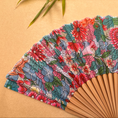 Floral patterned hand fan with a pink tassel on a gray background