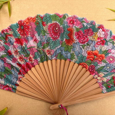 Floral patterned hand fan with a pink tassel on a gray background