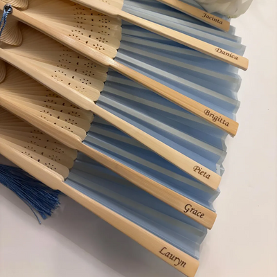 Personalised bamboo and silk hand fans with blue fabric, each engraved with bridesmaid names, perfect for weddings or events