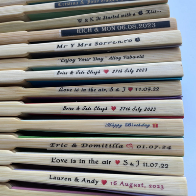 Close-up of custom printed bamboo hand fans with wedding names and dates on the main rib.
