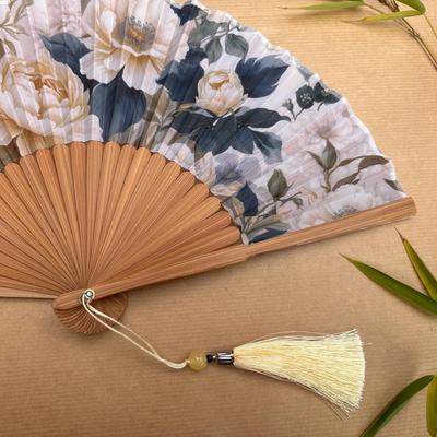 Floral-patterned hand fan with a tassel on a wooden surface