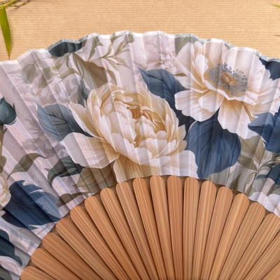 Floral-patterned hand fan with a tassel on a wooden surface