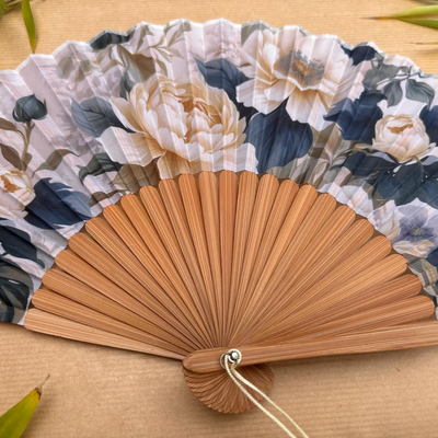 Floral-patterned hand fan with a tassel on a wooden surface