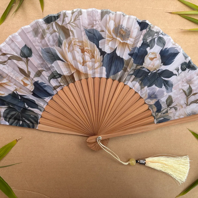 Floral-patterned hand fan with a tassel on a wooden surface