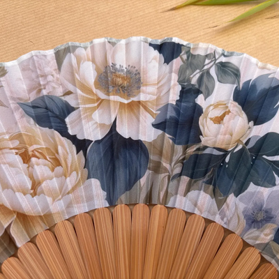 Floral-patterned hand fan with a tassel on a wooden surface