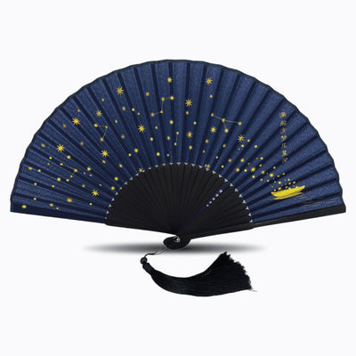 Navy blue silk folding hand fan featuring a constellation and starry night design in gold, with black bamboo ribs and a matching black tassel