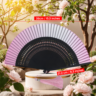 Pink folding hand fan with hollow-carved bamboo ribs and pink tassel, displayed open with size dimensions in a floral outdoor setting