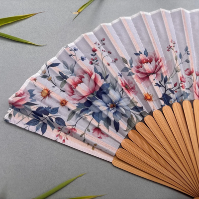 Floral-patterned hand fan with wooden frame and pink tassel on a gray background