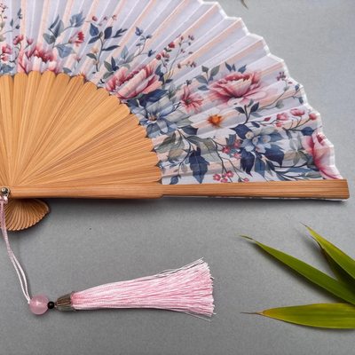 Floral-patterned hand fan with wooden frame and pink tassel on a gray background