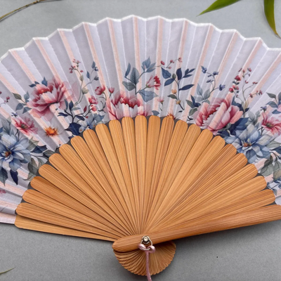 Floral-patterned hand fan with wooden frame and pink tassel on a gray background