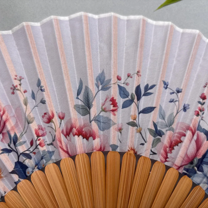 Floral-patterned hand fan with wooden frame and pink tassel on a gray background