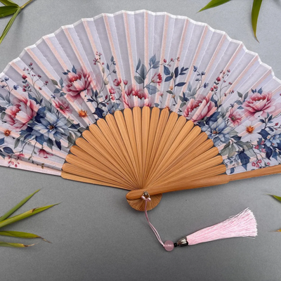 Floral-patterned hand fan with wooden frame and pink tassel on a gray background