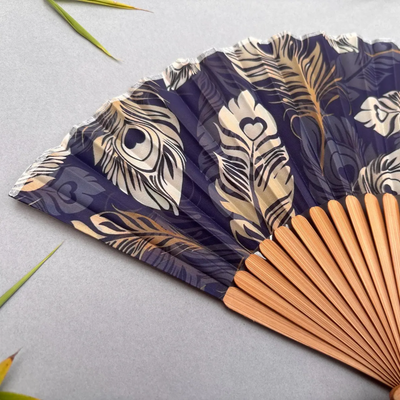 Handheld fan with peacock feather pattern on a gray background