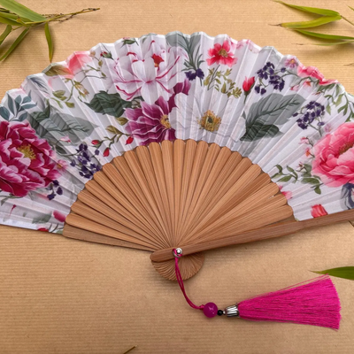 Floral-patterned hand fan with wooden frame and pink tassel on a beige background