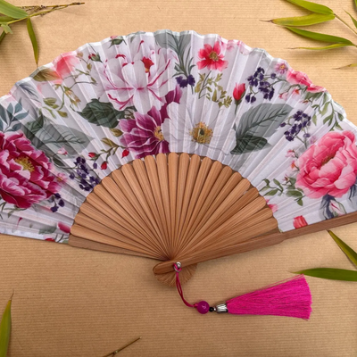 Floral-patterned hand fan with wooden frame and pink tassel on a beige background