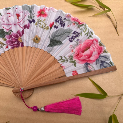 Floral-patterned hand fan with wooden frame and pink tassel on a beige background
